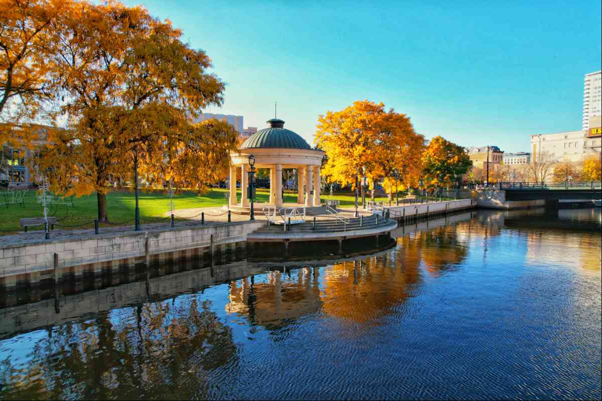 Gazebo on riverbank with autumn trees.